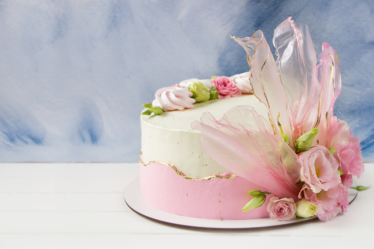 Un gâteau élégant orné de pétales ondulés en feuille de riz teintée et dorée, entouré de délicates fleurs fraîches, donnant l'impression d'une floraison printanière sur le dessert.