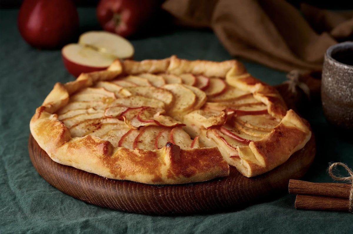 Tarte rustique aux pommes dorées, parfumée à la cannelle, servie tiède sur une assiette en bois automnale