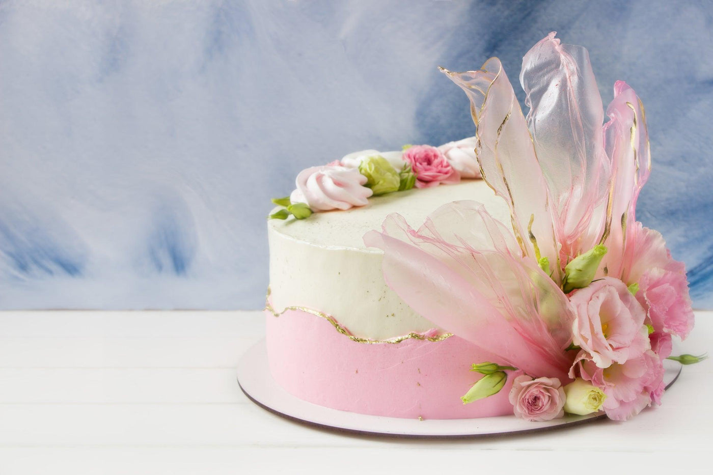 Un gâteau élégant orné de pétales ondulés en feuille de riz teintée et dorée, entouré de délicates fleurs fraîches, donnant l'impression d'une floraison printanière sur le dessert.