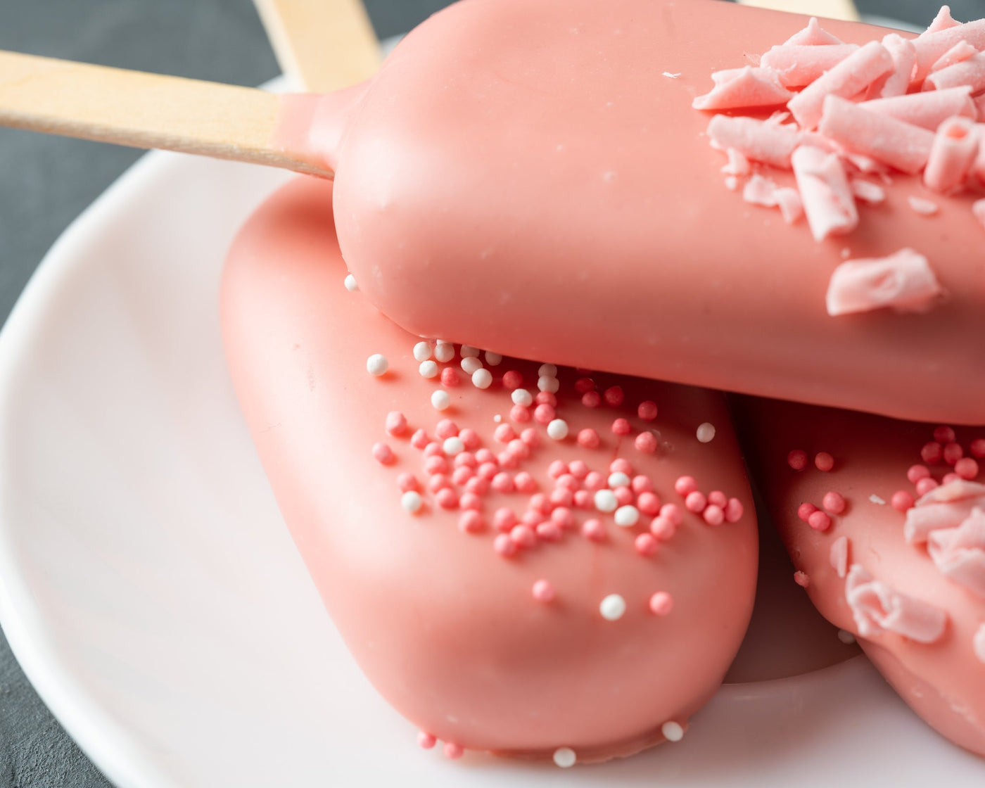 Magnum Cakes décorés de manière festive avec un enrobage de chocolat blanc et des ornements de Noël, tels que des houx et des flocons de neige en sucre, posés sur une assiette blanche.