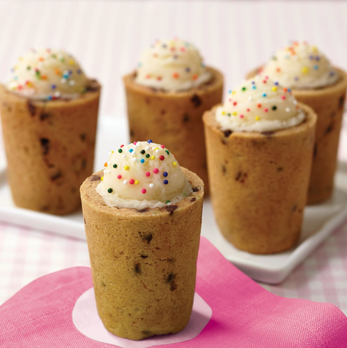 Des verres comestibles en forme de cookie garnis de crème et parsemés de vermicelles colorés, prêts à être savourés.